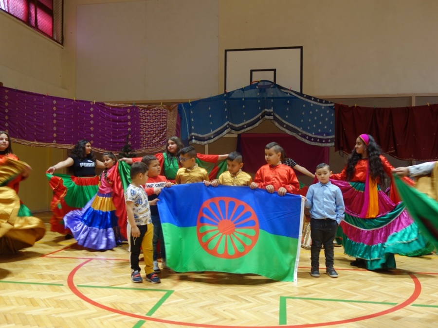 Zdjęcie przedstawia dzieci trzymające Flagę Romską podczas występu artystycznego
